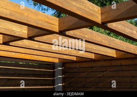 Vue rapprochée de poutres en bois altérées formant une structure de pergola avec la lumière du soleil et des ombres Banque D'Images