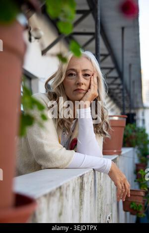 Femme mature réfléchie appuyée sur le balcon avec des fleurs Banque D'Images