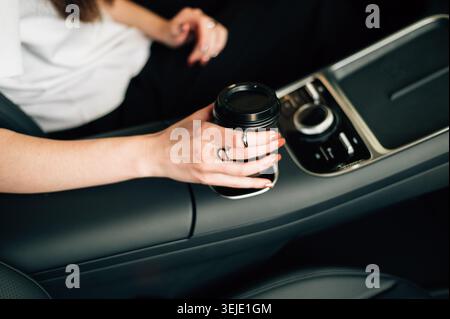 La main d'une fille tenant un verre de café dans une voiture. Photo de haute qualité Banque D'Images