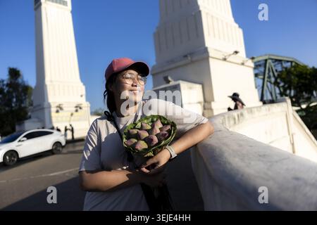 Heureuse femme thaïlandaise profitant de vacances à Bangkok montrant un sourire joyeux appuyé contre le pont blanc tenant beau bouquet de fleurs de lotus fraîches Banque D'Images