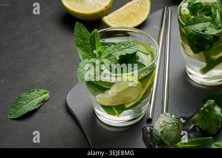 Verre de cocktail mojito avec des feuilles de menthe fraîche, des tranches de citron vert et des glaçons sur un fond de pierre sombre. Boisson estivale rafraîchissante Banque D'Images