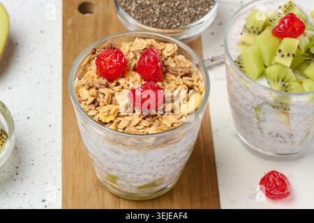 Yaourt et pudding aux graines de chia dans un verre, morceaux de kiwi. Table blanche Banque D'Images