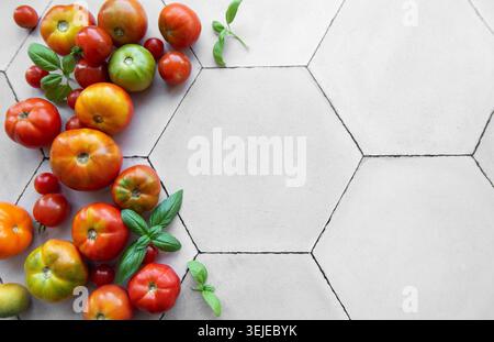 Tomates fraîchement récoltées et basilic dispersés sur une surface de cuisine carrelée hexagonale pendant l'été Banque D'Images