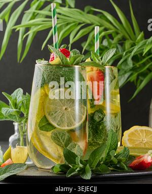 Une boisson rafraîchissante dans un verre avec des tranches de citron, des fraises, des feuilles de menthe fraîche et de l'eau pétillante Banque D'Images