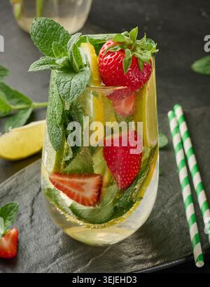 Une boisson rafraîchissante dans un verre avec des tranches de citron, des fraises, des feuilles de menthe fraîche et de l'eau pétillante Banque D'Images