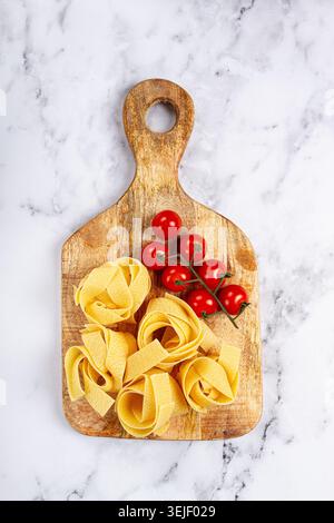 Pâtes pappardelle crues, sur une planche à découper en bois, avec tomates cerises, vue de dessus, pas de gens, Banque D'Images