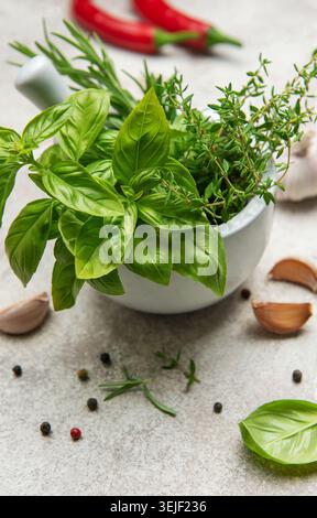 Herbes fraîches et épices dans le mortier avec pilon sur la table de cuisine Banque D'Images