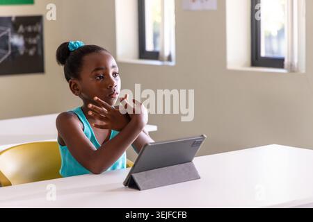 Fille afro-américaine d'âge scolaire assise dans la salle de classe portant turquoise tank scrunchie à l'aide d'une tablette Banque D'Images