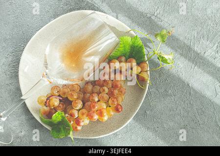 Une branche de raisins blancs, sur une plaque grise, avec un verre de vin blanc, vue de dessus, lumière naturelle, concept de nourriture, pas de gens, Banque D'Images
