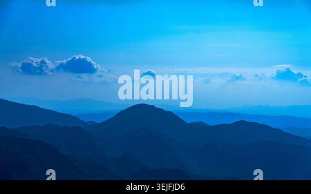 Ridges de montagne en couches sous un ciel bleu brumeux avec des nuages dispersés Banque D'Images