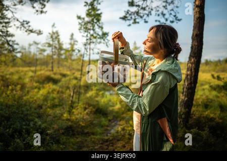 Fourragère femelle satisfaite avec un panier complet de champignons comestibles dans les bois d'automne ensoleillés le week-end Banque D'Images