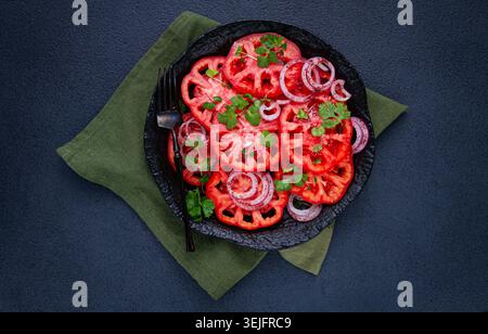 Tomates fraîchement tranchées et oignons rouges, garnis d'herbes, sur une assiette noire, salade d'été, pas de gens Banque D'Images
