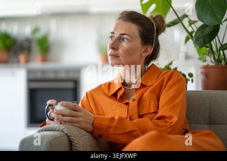 Pensant profondément contemplative femme d'âge moyen appréciant un moment calme à la maison avec tasse à café Banque D'Images