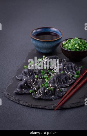 Boulettes de gyoza japonais, faites de pâte noire, gyoza noir, avec oignons verts et sauce, sur une assiette, gros plan, Banque D'Images