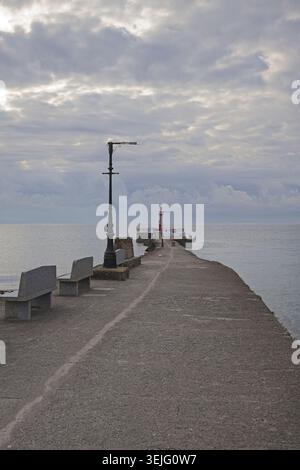 Lumière matinale nuageuse sur le ponton Banjo Looe Cornwall, bancs et lampadaire menant à la mer sous un ciel nuageux Banque D'Images
