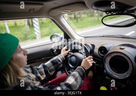Femme conduisant la voiture, assise sur le siège des conducteurs tenant le volant et regardant la route tout en roulant. Banque D'Images