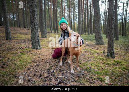 Femme heureuse caressant chien apaisant animal pendant la promenade dans la forêt de pins, liaison extérieure avec le propriétaire Banque D'Images