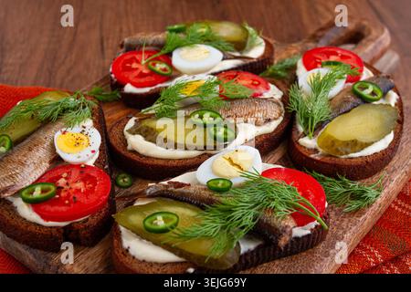 Sandwichs ouverts avec sprats, légumes et herbes, sur une planche de bois, petit déjeuner, collation, Banque D'Images