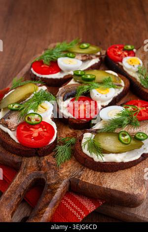 Sandwichs ouverts avec sprats, légumes et herbes, sur une planche de bois, petit déjeuner, collation, Banque D'Images