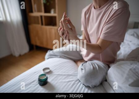 Femme d'âge moyen faisant des rituels de routine de beauté le matin, en appliquant la crème pour les mains du pot sur la peau. Banque D'Images