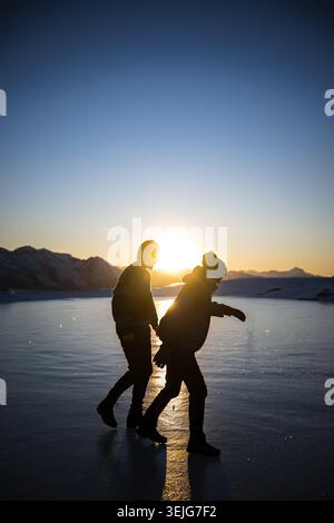 Deux personnes marchant sur un lac gelé au coucher du soleil à Kühtai, Tyrol, Autriche. Banque D'Images