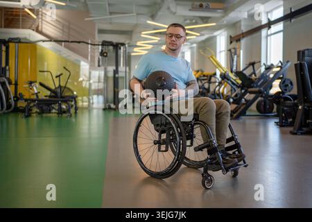 Homme handicapé en fauteuil roulant travaillant sur les bras et la force du tronc avec balle lourde Med à la séance de gymnastique. Banque D'Images