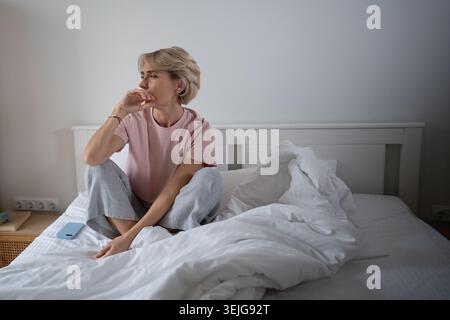 Femme endormie d'âge moyen assise dans le lit bâillant après une nuit agitée, expression fatiguée et paresseuse. Banque D'Images