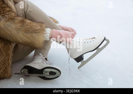 Gros plan de femme portant des patins blancs sur la patinoire en hiver. Femme attachant des lacets sur des patins Banque D'Images