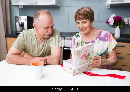 Mari aîné aimant offrant un cadeau à sa femme. Heureux couple aîné à la maison. Banque D'Images