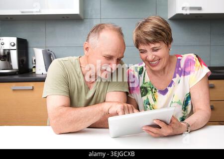 Heureux couple senior utilisant la tablette dans la cuisine à la maison Banque D'Images