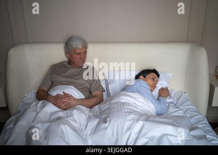Couple marié senior en conflit, homme et femme couchés dans le lit avec tension émotionnelle après bagarre. Banque D'Images