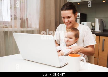 Maman et bébé. une jeune mère travaillant avec un ordinateur portable dans la cuisine. télétravailleurs. Travailler où que vous soyez. Banque D'Images