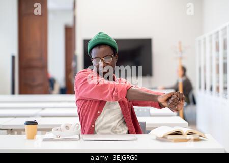 Un étudiant africain fatigué, qui étire les mains, détend l'esprit et les muscles après une étude intense en bibliothèque Banque D'Images