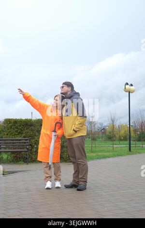 Heureux couple marchant dans le parc en jour de pluie Banque D'Images
