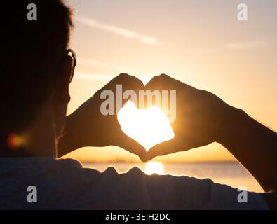 Mains d'homme formant une forme de coeur avec silhouette de coucher de soleil Banque D'Images