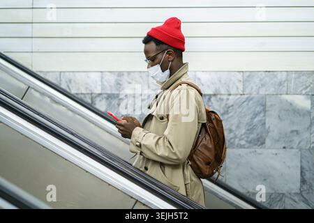 Homme noir se tient sur l'escalator dans le métro, porter un masque facial pour se protéger du contact avec le virus de la grippe Banque D'Images
