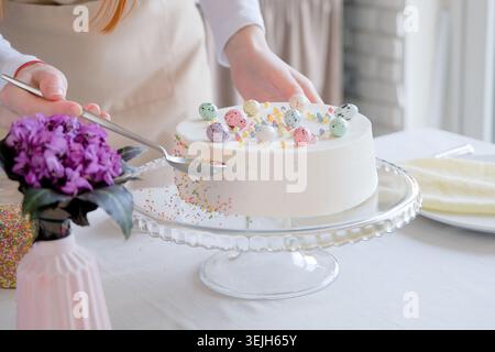 Jeune femme faisant gâteau de Pâques dans des couleurs pastel dans la cuisine, décorer avec des saupoudres Banque D'Images