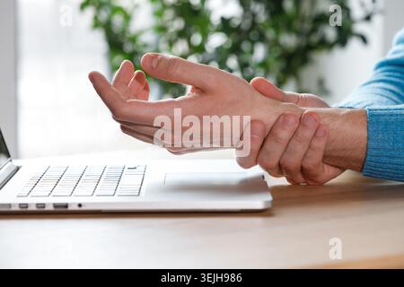 Gros plan des bras de l'homme tenant son poignet douloureux causé par un travail prolongé sur l'ordinateur, ordinateur portable. Syndrome du canal carpien, artrite Banque D'Images