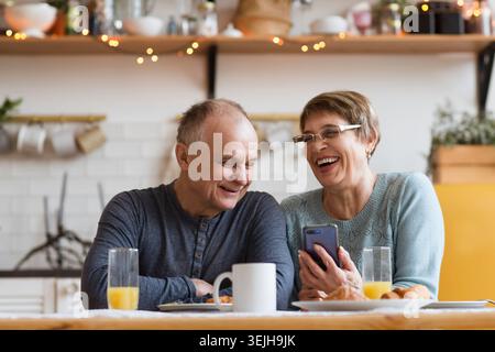 Couple senior prenant le petit déjeuner et utilisant un smartphone à la maison Banque D'Images