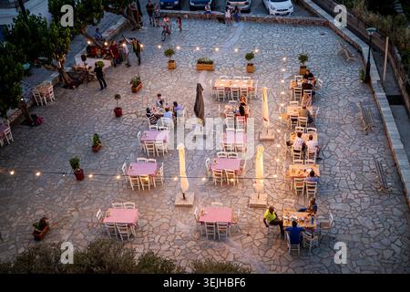 Les couples et les amis apprécient un dîner en plein air détendu sur une terrasse en pierre au crépuscule, avec nappes à carreaux, jeux de lumières et plantes en pot créant un wa Banque D'Images