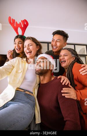 Divers amis portant serre-tête en bois et chapeau de Père Noël prenant selfie dans le salon avec smartphone. Festif, camaraderie, célébrité Banque D'Images