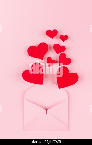 Enveloppe de papier ouverte avec des coeurs rouges comme message d'amour sur fond de couleur rose doux. Concept de Saint-Valentin pour le design. Banque D'Images
