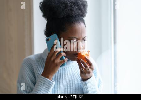 Femme noire malade essayant de sentir l'odeur de la moitié fraîche orange mandarine parlant au téléphone. COVID-19 Banque D'Images
