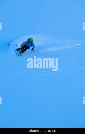 Un skieur sculpte dans la poudre fraîche avec des équipements vibrants, pulvérisant de la neige sous un ciel bleu vif. Le mouvement rapide et contrôlé transmet l'énergie, la compétence, et Banque D'Images