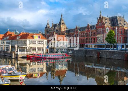 Amsterdam, pays-Bas – 16 mai 2026 : vue panoramique au lever du soleil sur la gare centrale d'Amsterdam et les bateaux sur le canal reflétés dans les eaux calmes de l'Amstel Can Banque D'Images