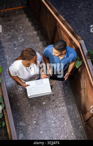 Divers collègues debout sur un palier d'escalier carrelé de pierre examinant le contenu sur ordinateur portable et tablette. Collaboration, travail d'équipe, WOR Banque D'Images
