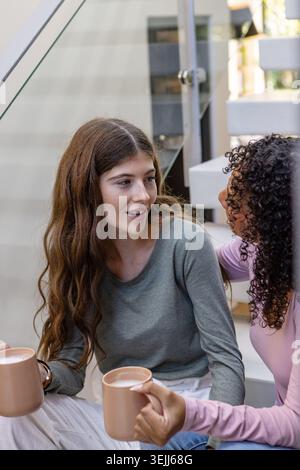 Divers amis féminins tenant des tasses et discutant sur un atterrissage moderne à la maison. Amitié, informel, confortable, intérieur, moderne, rela Banque D'Images