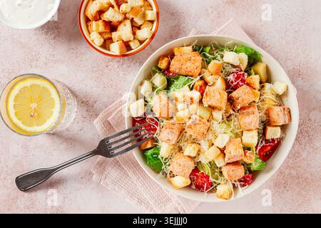 Salade César au saumon, avec croûtons et vinaigrette, dans un saladier, sur une table rose, Banque D'Images