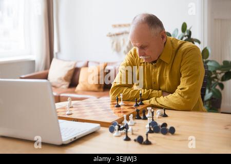 Vieil homme senior jouant au jeu d'échecs sur le plateau d'échecs, jeu en ligne avec un ami, appel vidéo en raison de la distanciation sociale à la maison Banque D'Images