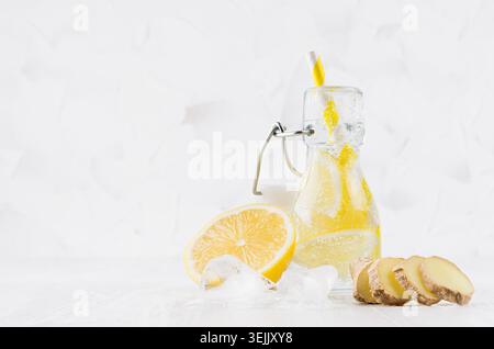 Boisson maison d'été - eau de citron infusée avec des glaçons, gingembre, tranches, soda, paille dans une bouteille de yoke en blanc léger doux inter Banque D'Images